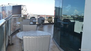 A rooftop terrace with wicker furniture, a glass balustrade, and a city view. - GV Tower Hotel (Cebu City)