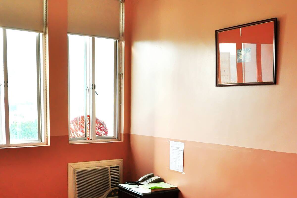 A bedroom with a bed, a window, a wall-mounted phone, and a radiator.