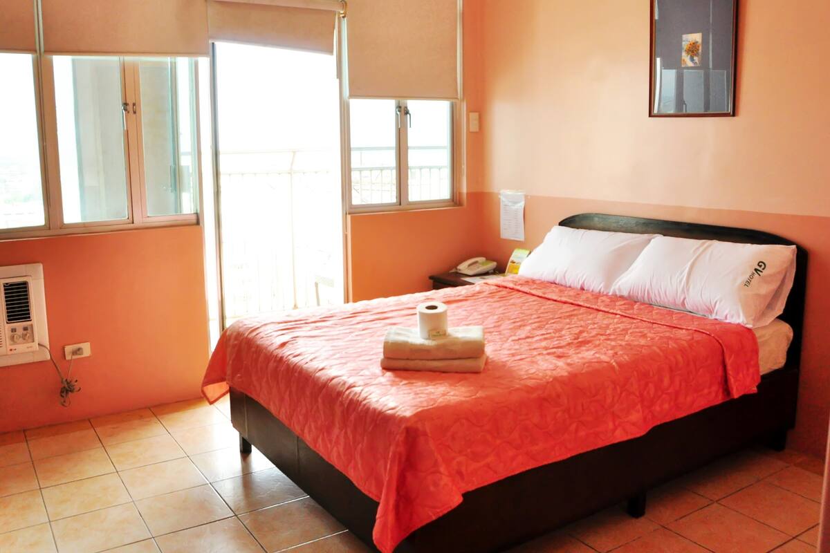 A bedroom with a bed, a window, a wall-mounted phone, and a wall-mounted air conditioner.