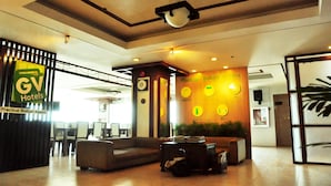 A hotel lobby with a reception desk, seating area, and a wall with clocks and a TV. - GV Tower Hotel (Cebu City)