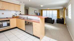 A modern kitchen with a dishwasher, oven, and a sink. There is a living area with a sofa and a TV. - Springwood Tower Apartment Hotel (Springwood)