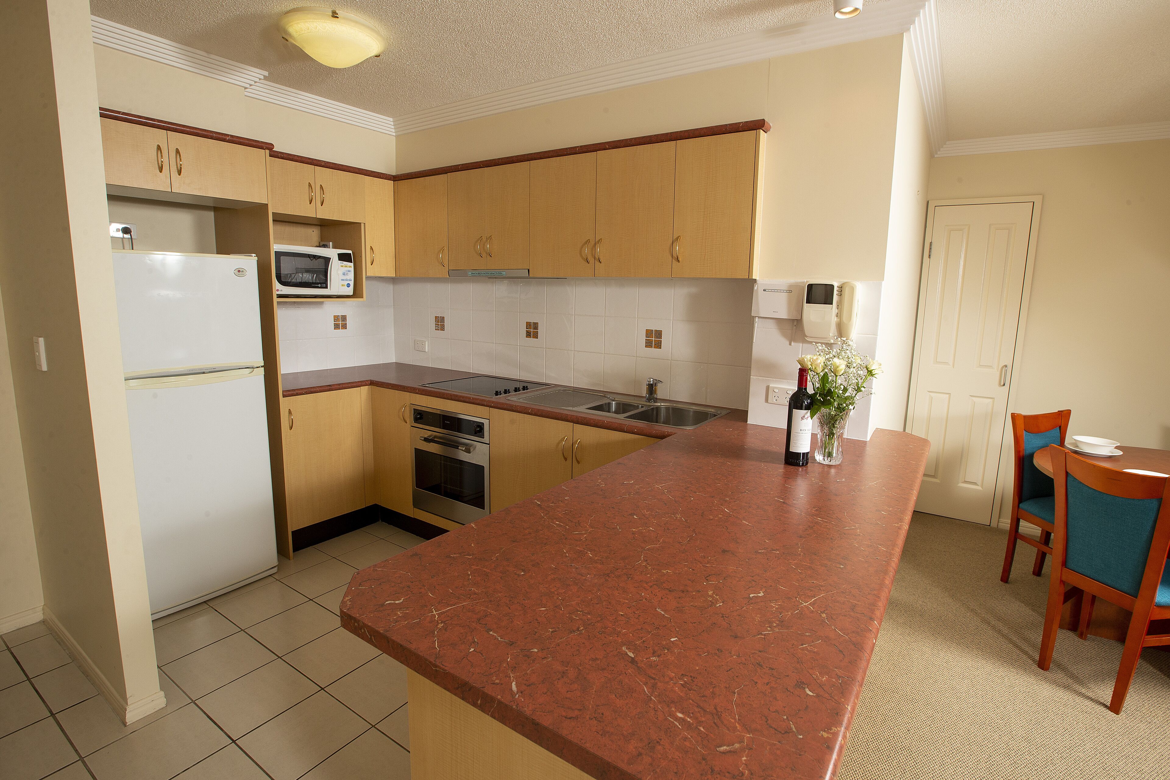 A kitchen with wooden cabinets, a refrigerator, a microwave, a sink, and a dining area with chairs and a table.
