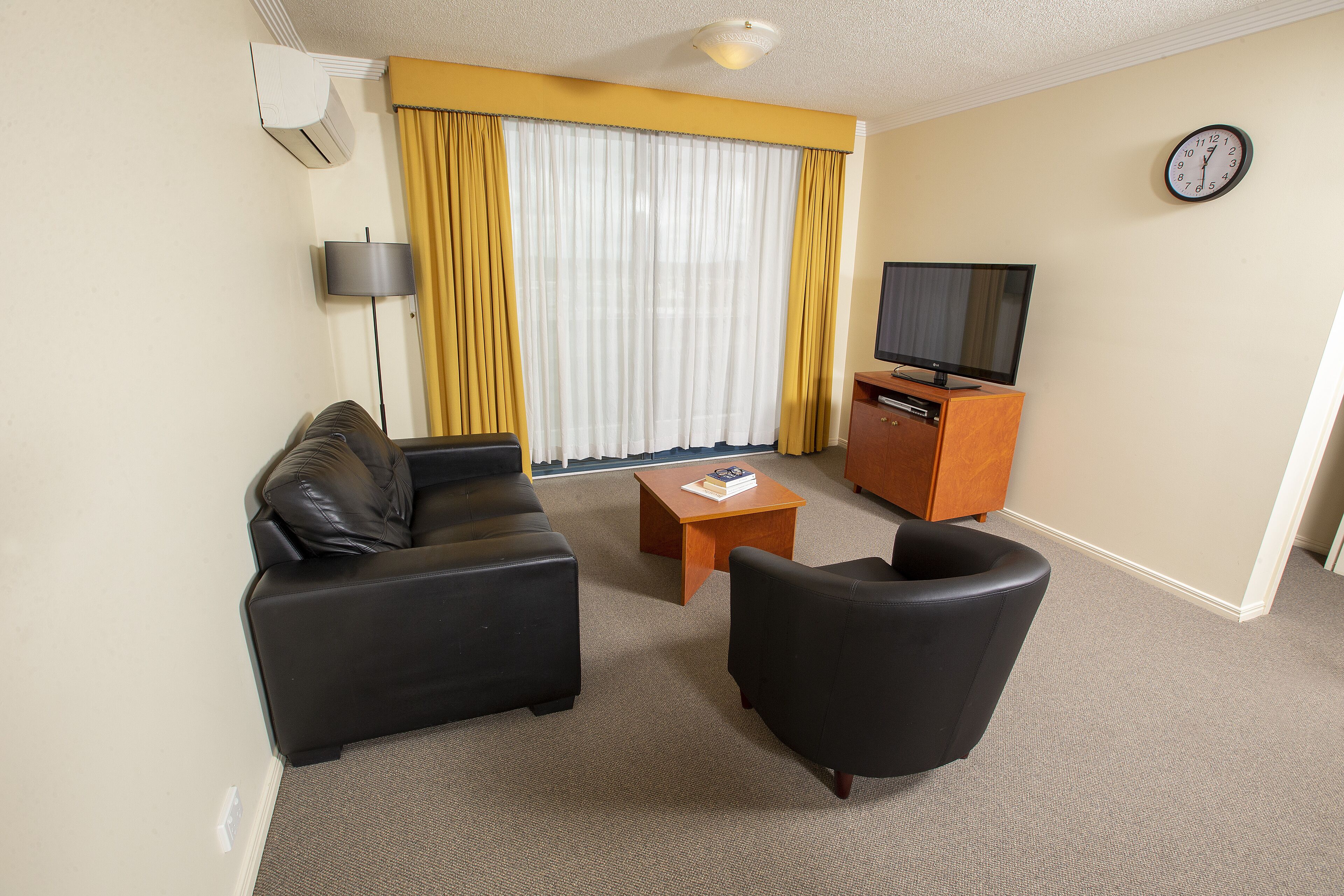 Una sala de estar con sofá, sillón, mesa de centro, televisor y cortinas.