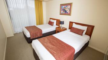 A hotel room with two beds, a nightstand, a lamp, a painting on the wall, and a window with curtains.