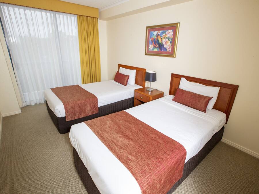 A hotel room with two beds, a nightstand, a lamp, a painting on the wall, and a window with curtains.