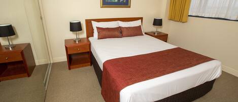 A hotel room with a large bed, two bedside tables with lamps, a framed artwork on the wall, and a window with curtains.