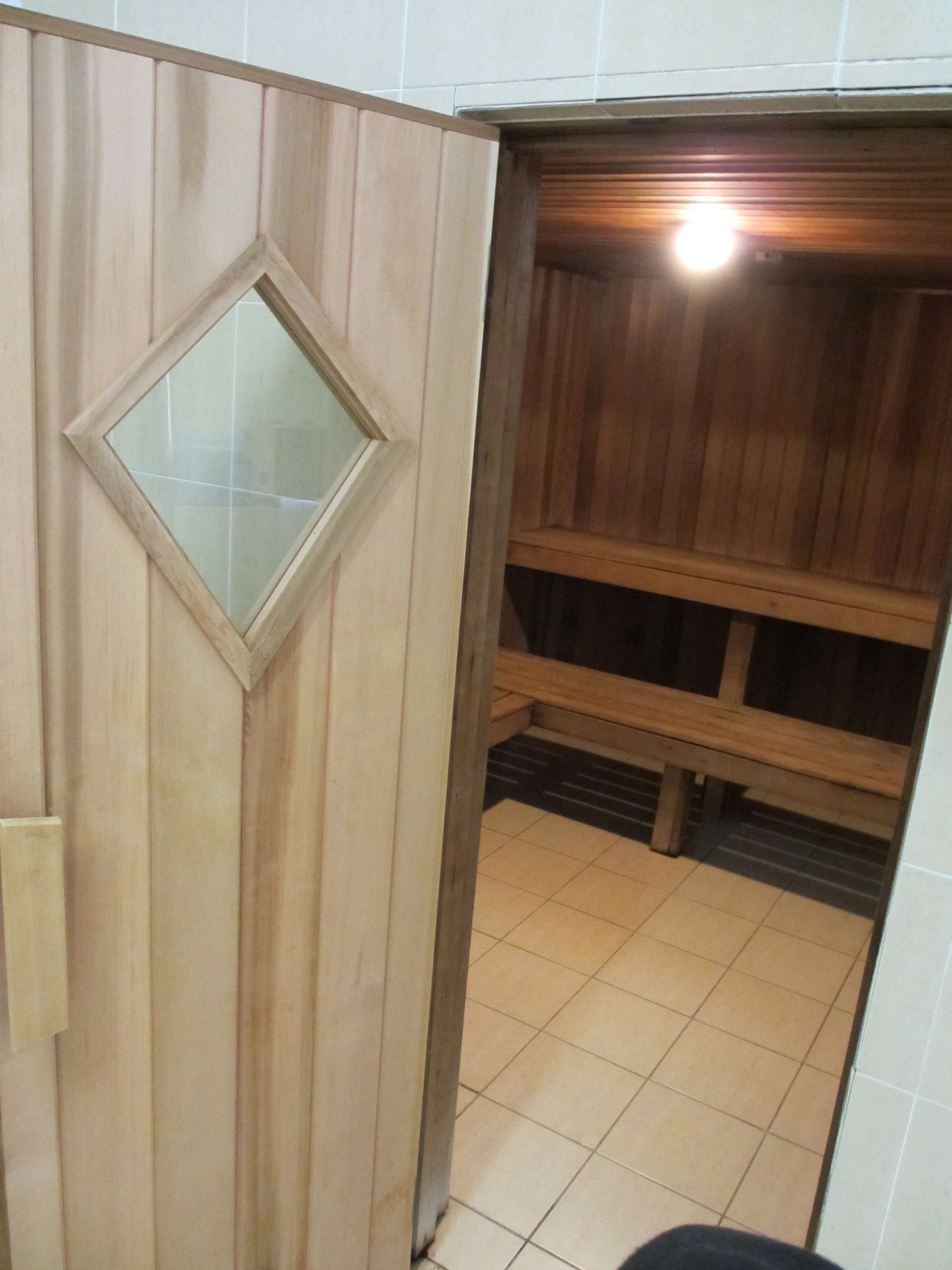 A wooden door with a glass panel, leading to a room with a tiled floor and a wooden bench.