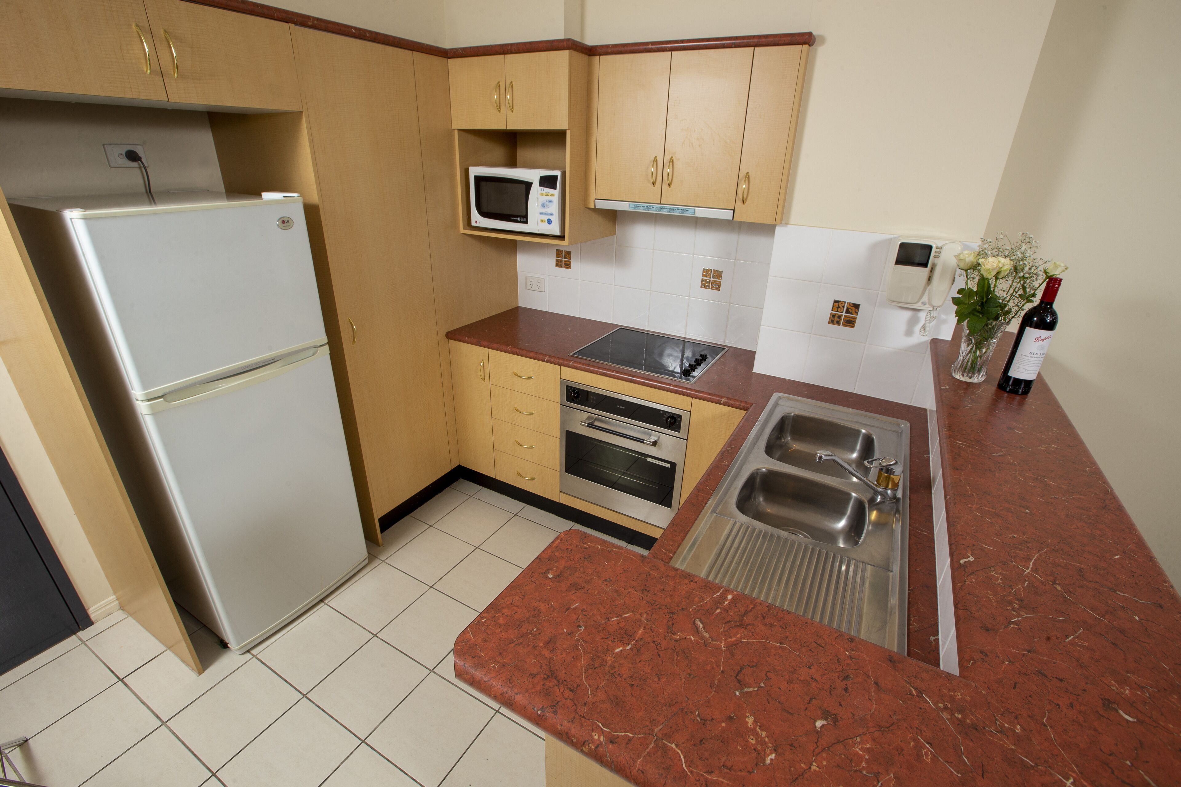 Una cocina con refrigerador, microondas, horno, lavaplatos y una botella de vino.