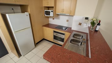 A kitchen with a refrigerator, microwave, oven, sink, and a wine bottle.