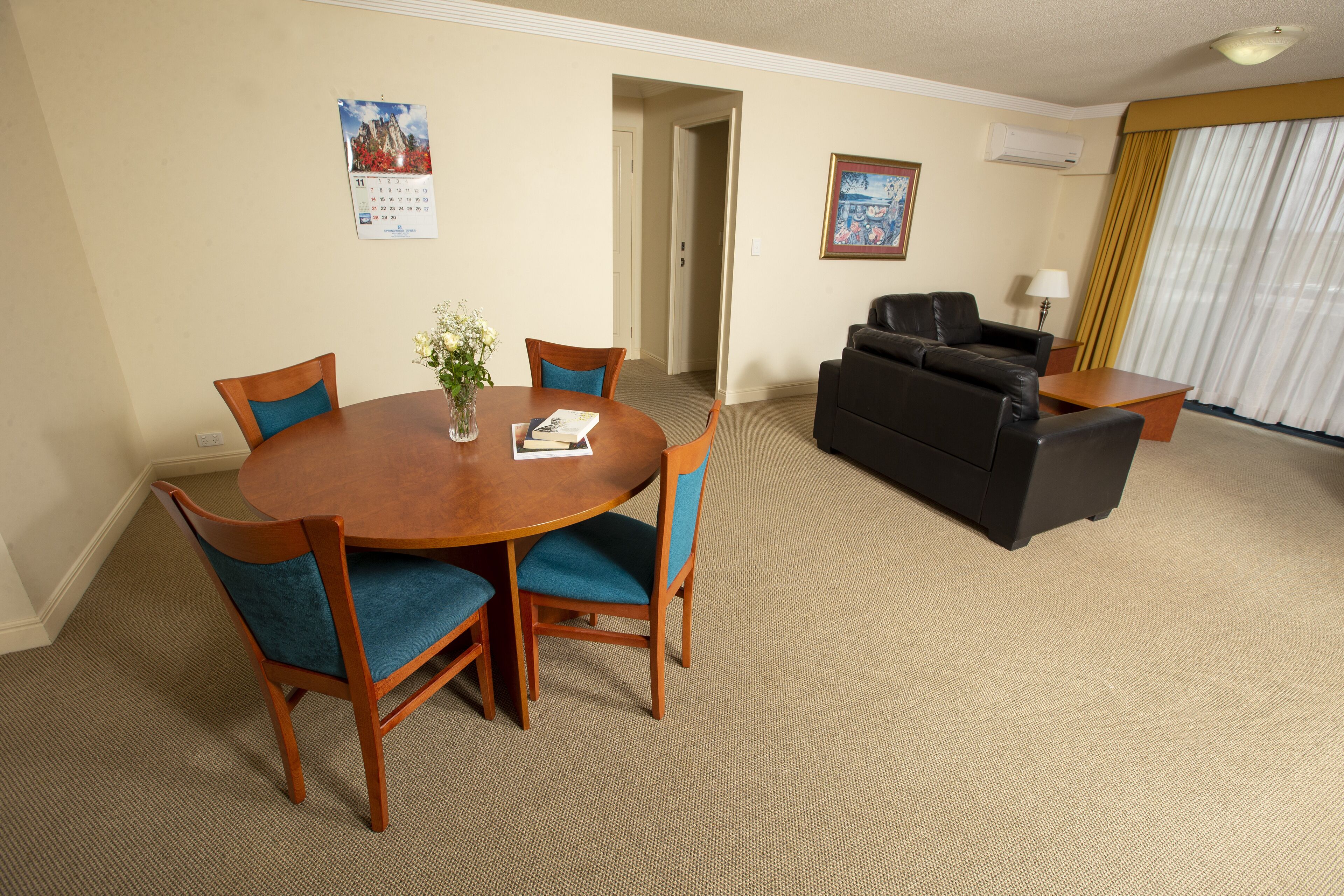 A hotel room with a dining table, chairs, a sofa, and a lamp.