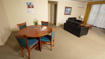 A hotel room with a dining table, chairs, a sofa, and a lamp.