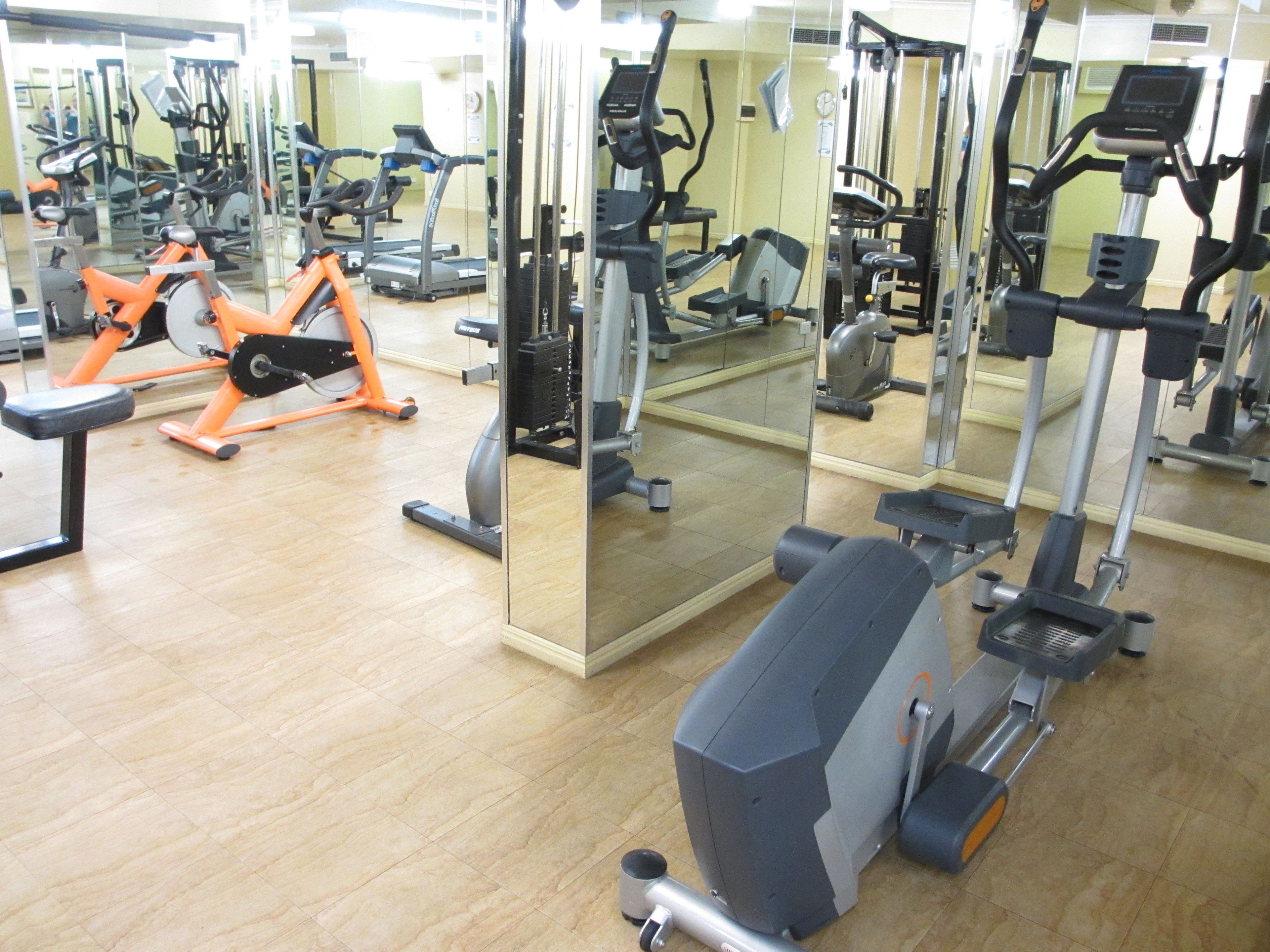 A gym with various exercise machines, including treadmills and weight equipment, and a large mirror wall.