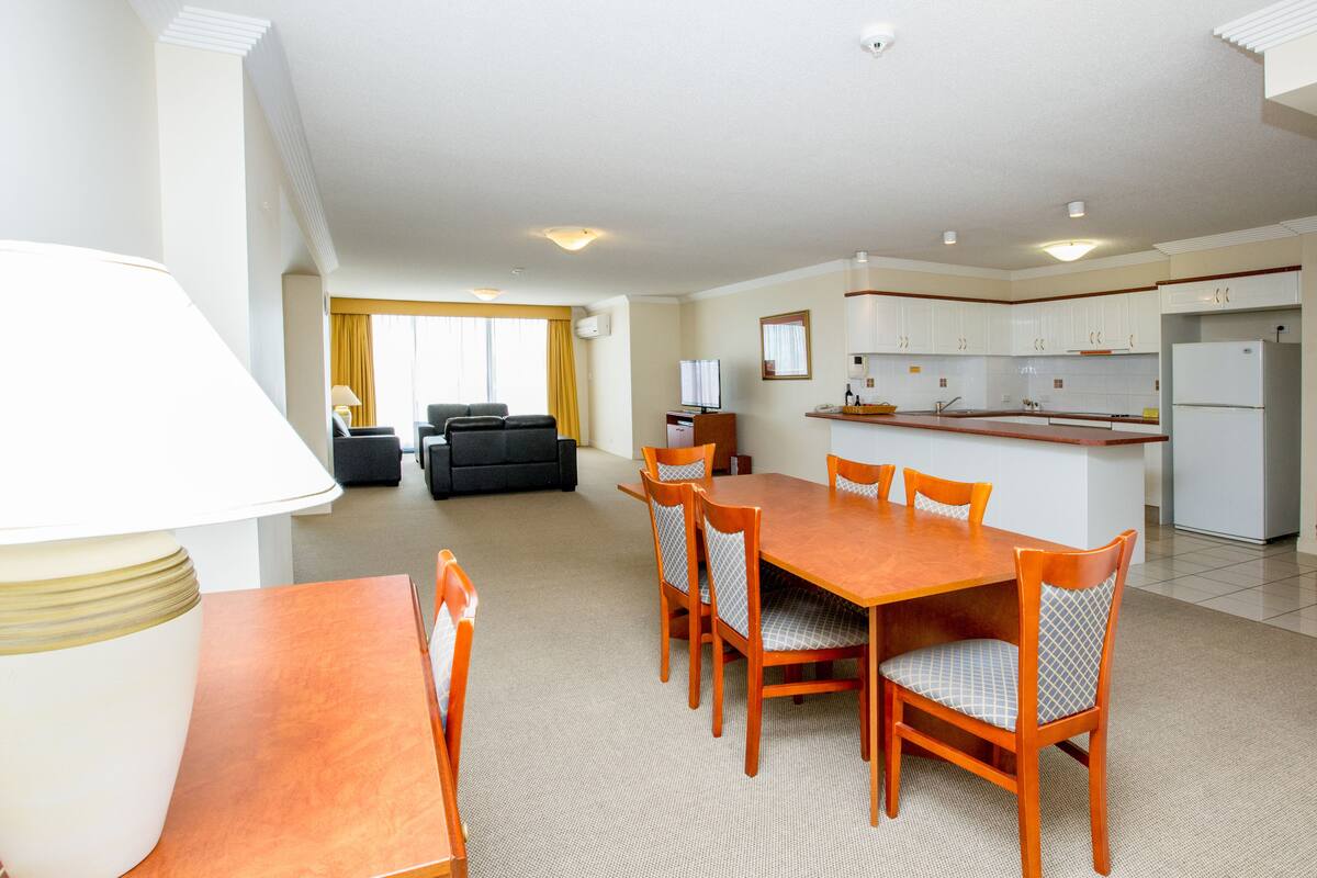 Una habitación de hotel moderna con comedor, kitchenette y sala de estar con sofá y televisor.