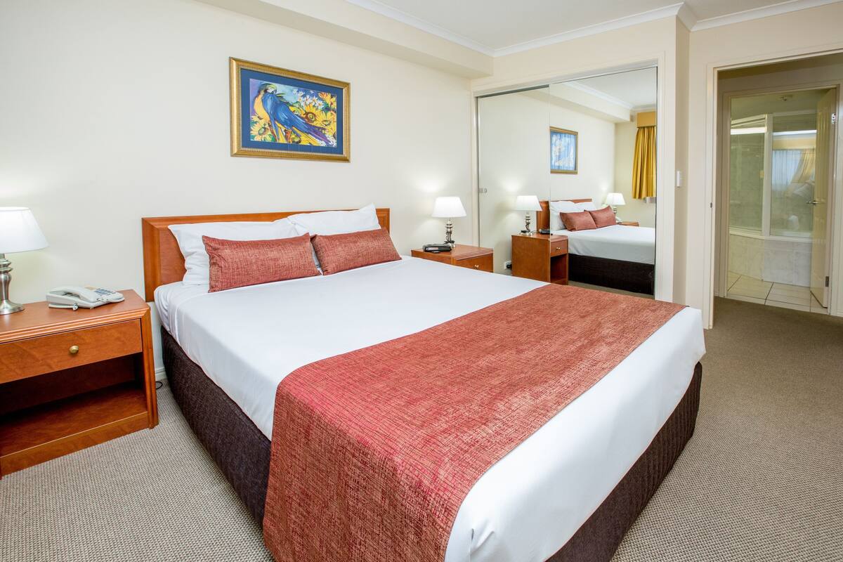 Una habitación de hotel con una cama grande, mesitas de noche, un tocador, un espejo y un cuadro en la pared.