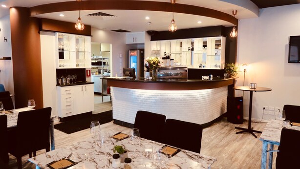 A restaurant with a curved counter, white brick walls, and black chairs. - Springwood Tower Apartment Hotel (Springwood)