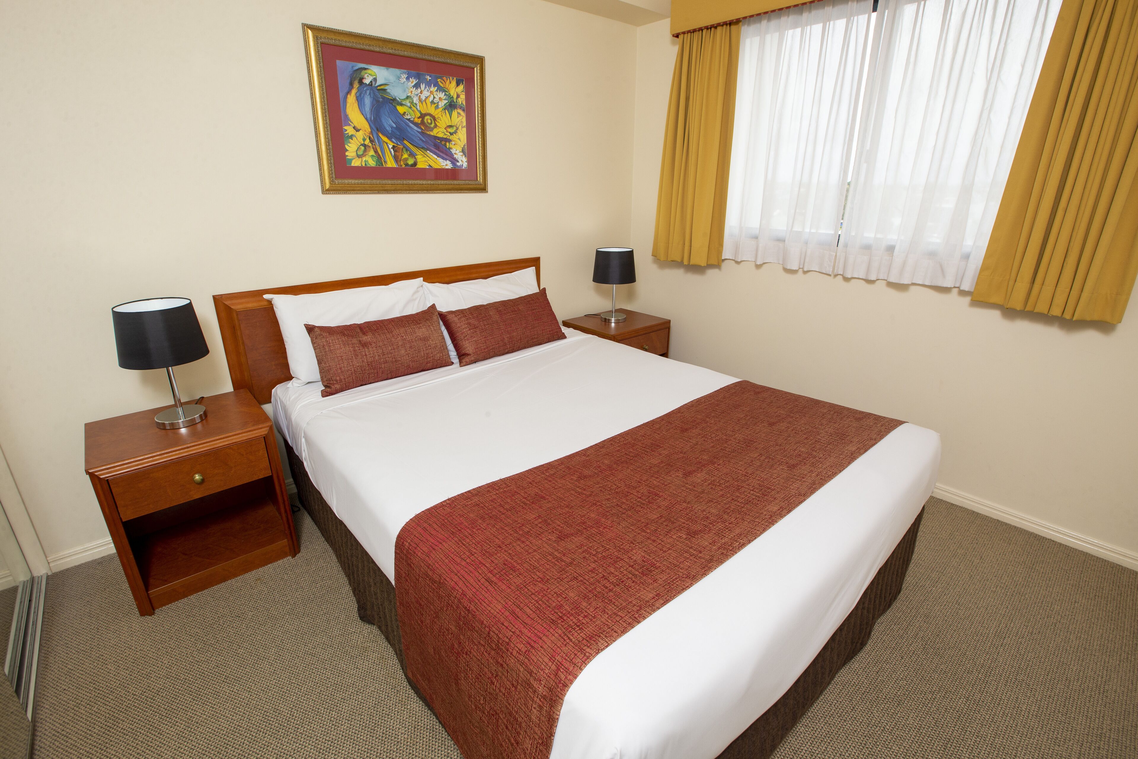 A hotel room with a large bed, wooden nightstands, a lamp, a painting, and a window with curtains.