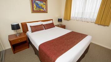 A hotel room with a large bed, wooden nightstands, a lamp, a painting, and a window with curtains.