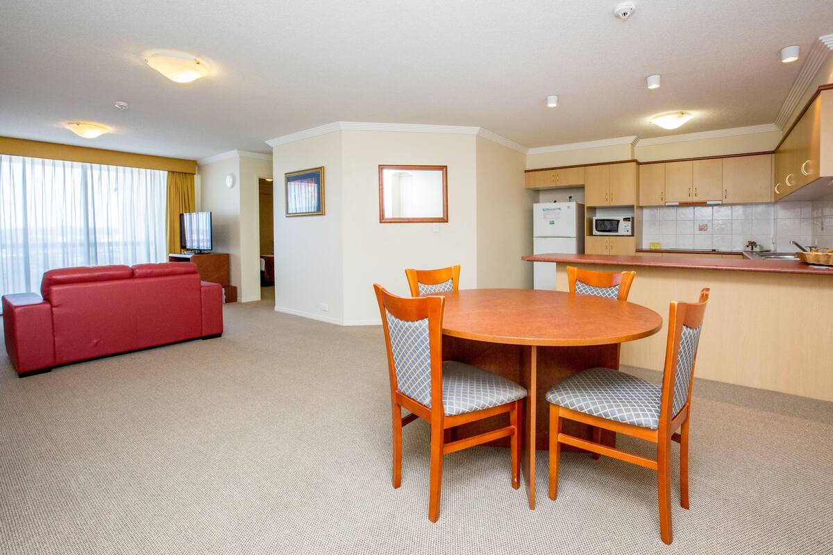 Un espacio habitable compacto con zona de comedor, kitchenette y un sofá rojo.