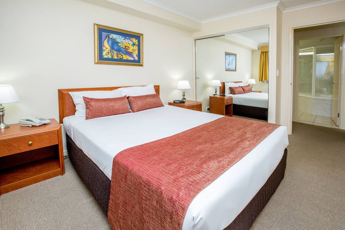 Habitación de hotel con una cama grande, mesitas de noche, un espejo y un cuadro en la pared.