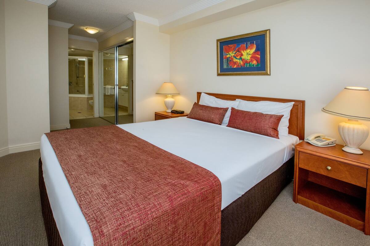 Habitación de hotel con una cama grande, una mesita de noche con lámpara, un teléfono y un cuadro en la pared.