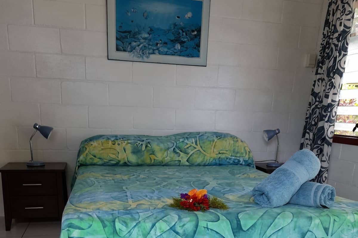 A bedroom with a bed, two bedside tables, a nightstand, a wall-mounted painting, and a window with curtains.