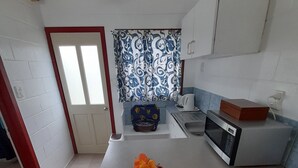A kitchen with a central island, a microwave, a kettle, and a flower on the island.