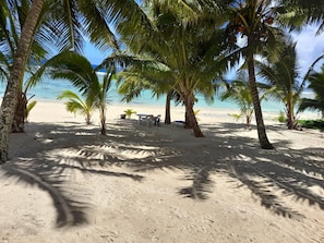A beach with palm trees and a table with chairs. - Reefcomber Sunset Beach (Rarotonga)