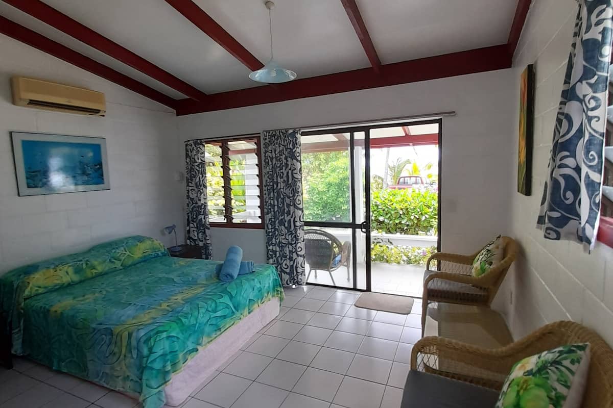 A room with a bed, two wicker chairs, a ceiling fan, and a view through a glass door.