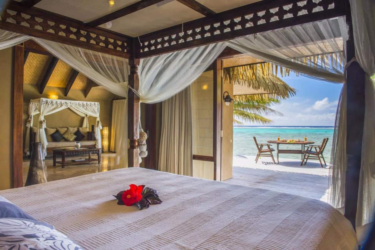 A bedroom with a bed, a nightstand, a table, and a view of the beach.