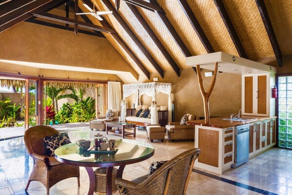 A spacious living area with a high ceiling, a dining table, comfortable seating, and a kitchen area. - Rumours Luxury Villas & Spa (Rarotonga)