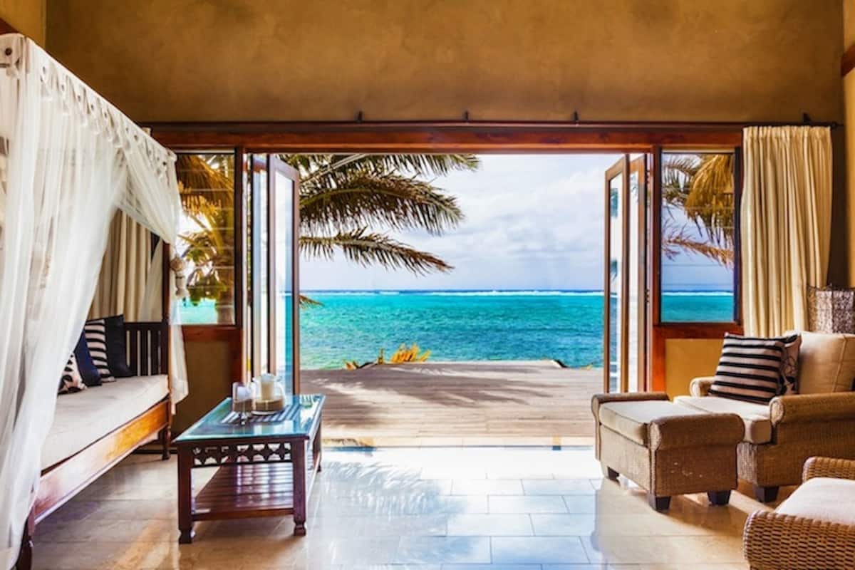 A room with a view of the ocean, a sofa, a coffee table, and wicker chairs.