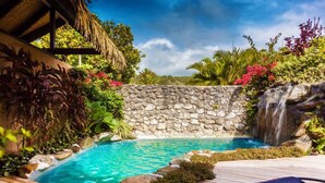A pool area with a stone wall, a waterfall, and lush greenery. - Rumours Luxury Villas & Spa (Rarotonga)