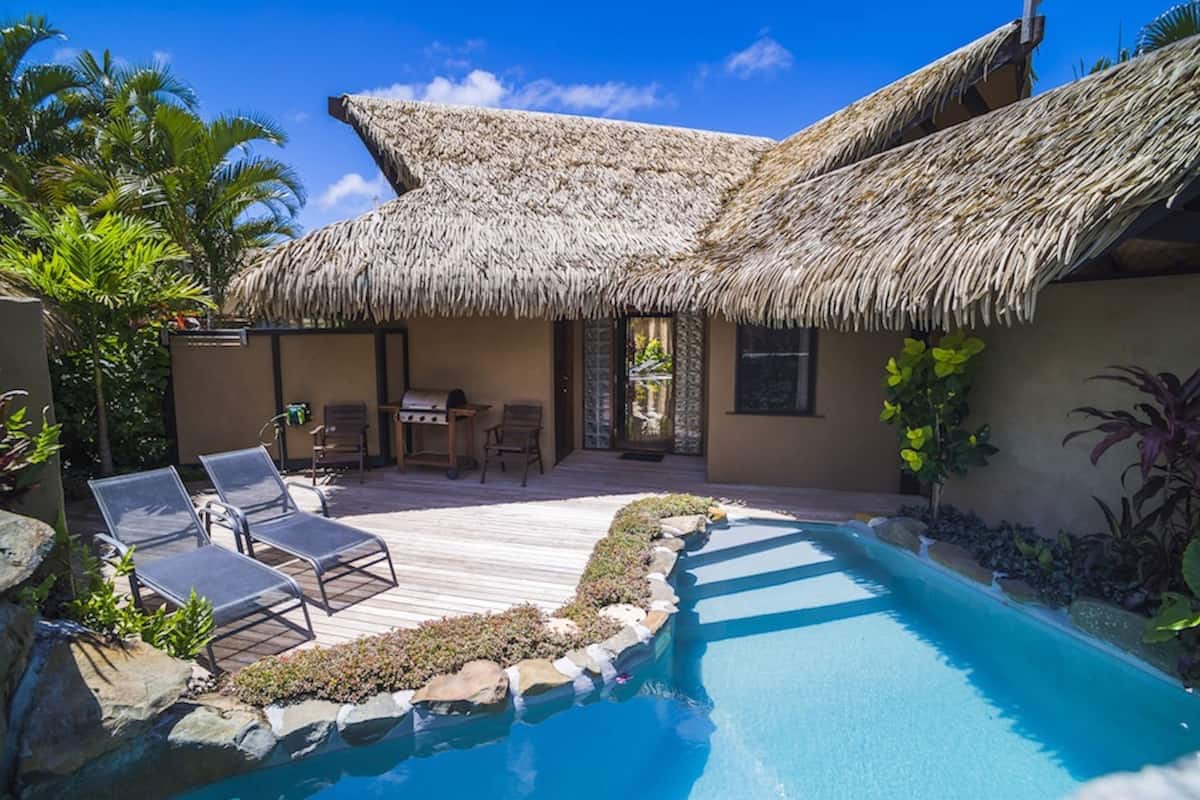 A poolside area with lounge chairs, a thatched-roof building, and a clear blue pool.
