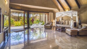 A spacious living area with a large glass door leading to a tropical garden, a comfortable sofa set, and a canopy bed. - Rumours Luxury Villas & Spa (Rarotonga)