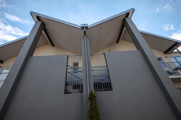 A modern building with a flat roof, two visible windows with metal bars, and a central vertical structure.