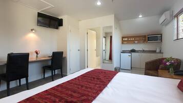 A hotel room with a bed, a desk with two chairs, a kitchenette, and a TV mounted on the wall.