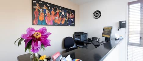 Uma receção com um vaso de flores, um relógio e um quadro de músicos na parede.
