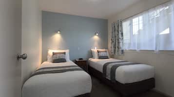 A bedroom with two single beds, a nightstand, a wall-mounted light, and a window with sheer curtains.