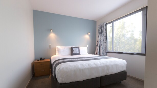 Een slaapkamer met een bed, nachtkastje en een raam met gordijnen.