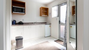 Een kleine keuken met witte kastjes, een magnetron, een spoelbak en een vuilnisbak.