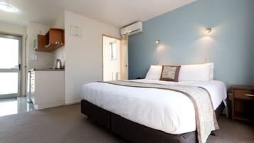 A bedroom with a large bed, a bedside table, a wardrobe, and an air conditioning unit.
