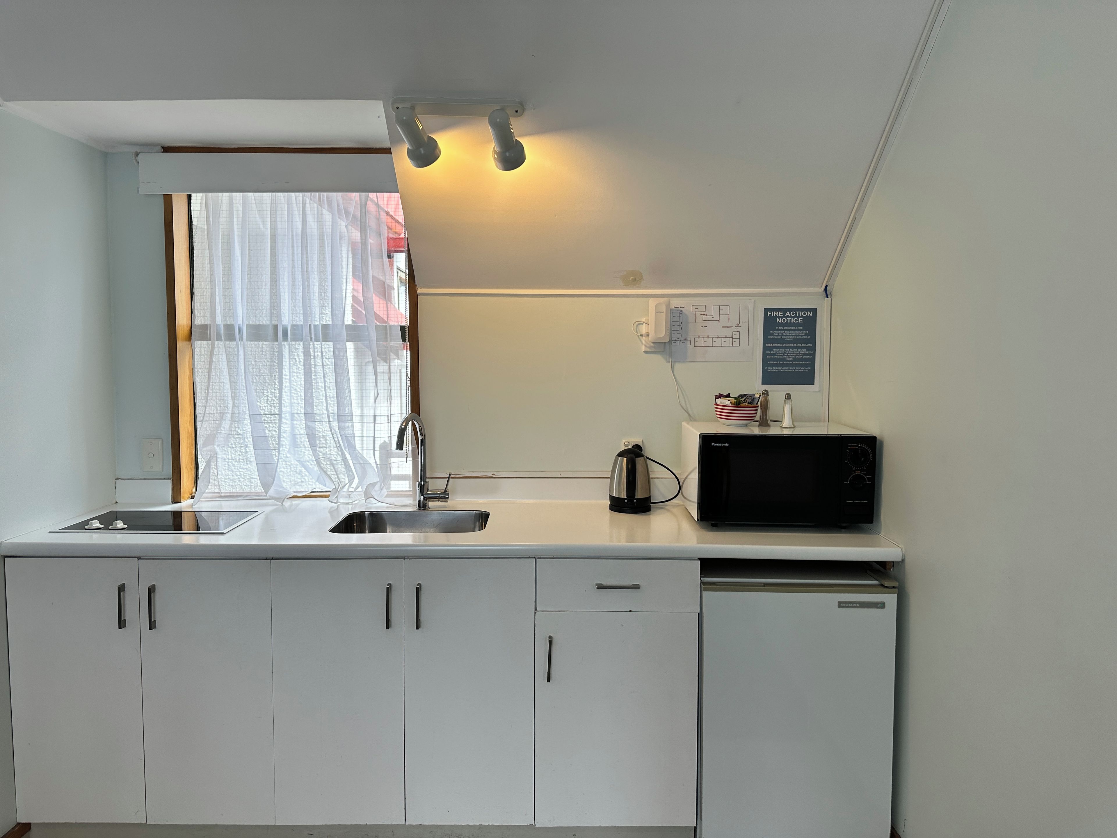 A kitchen with a sink, a kettle, a microwave, and cabinets.