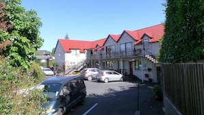 A row of two-story buildings with red roofs, parked cars, and a street lamp. - Owens Motel (Dunedin)