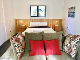 Quarto com cama, mesas de cabeceira, janela e um quadro na parede.