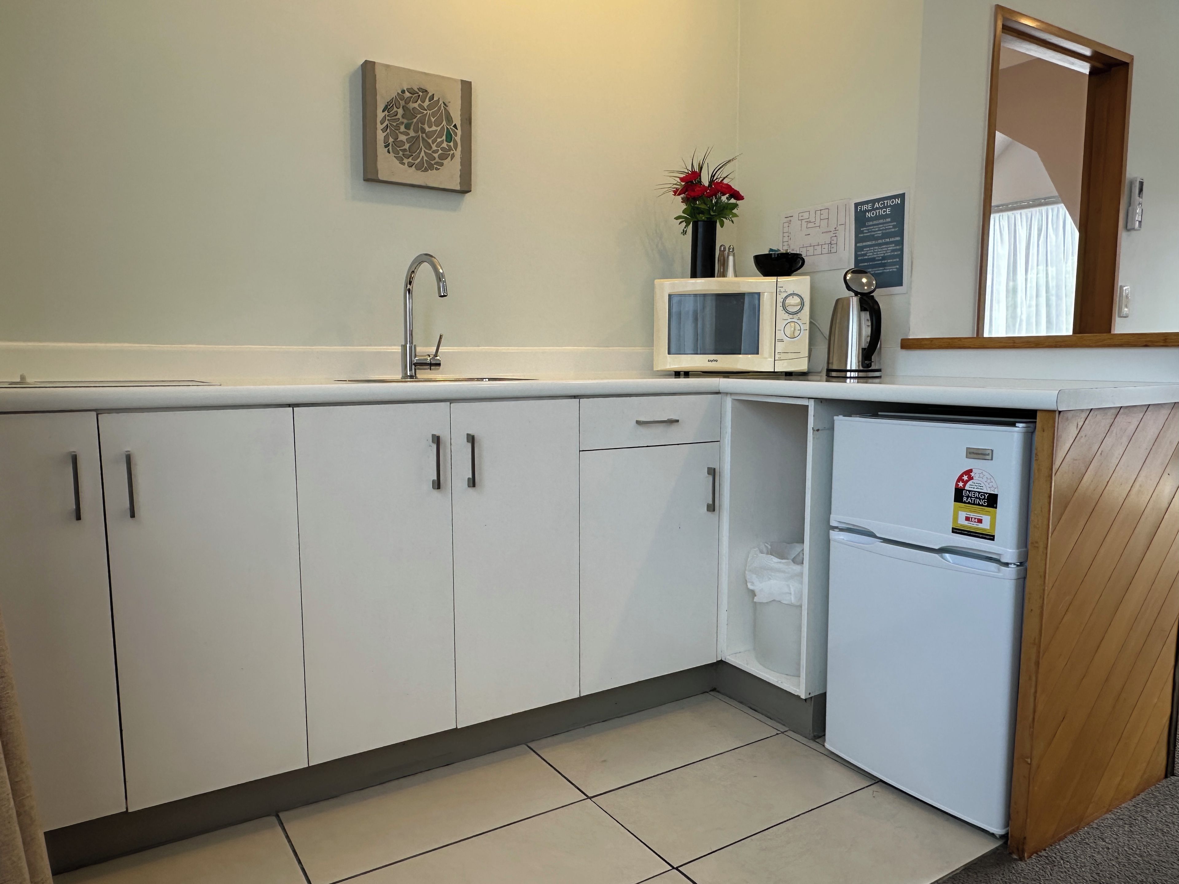 A kitchen with white cabinets, a microwave, a refrigerator, a sink, and a vase with flowers.