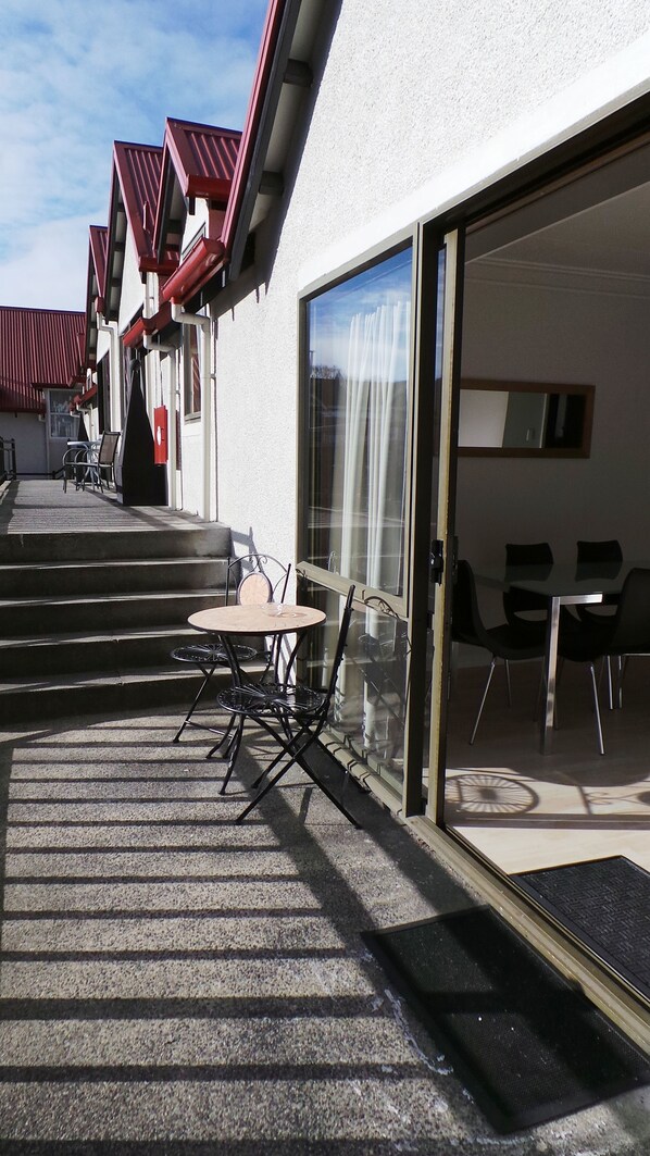 A hotel patio with outdoor seating, a staircase leading to the entrance, and a glass door entrance. - Owens Motel (Dunedin)