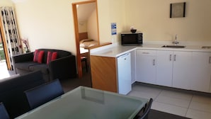 A compact living space with a kitchenette, a dining area, and a seating area with a sofa and chairs. - Owens Motel (Dunedin)