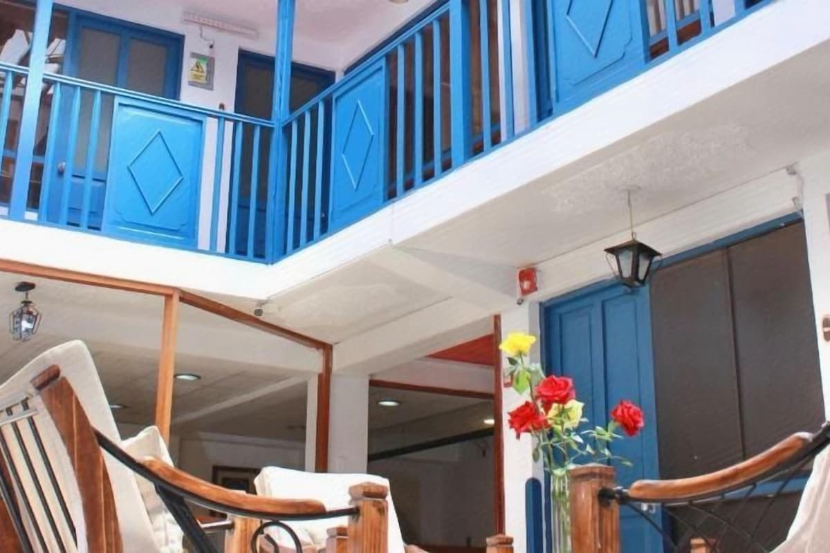 Una habitación de hotel con balcón, una silla de madera y un jarrón con flores.