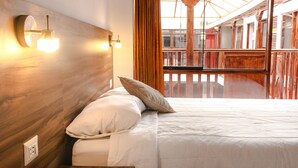 A bed with white linens and two pillows, a wooden headboard with wall-mounted lights, and a view of a balcony with wooden railings and a glass ceiling. - San Blas Plaza Inn (Cusco)