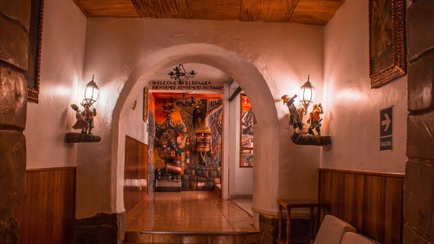 A hallway with a wooden ceiling, a bench, and a staircase leading to a room with a mural. - San Blas Plaza Inn (Cusco)